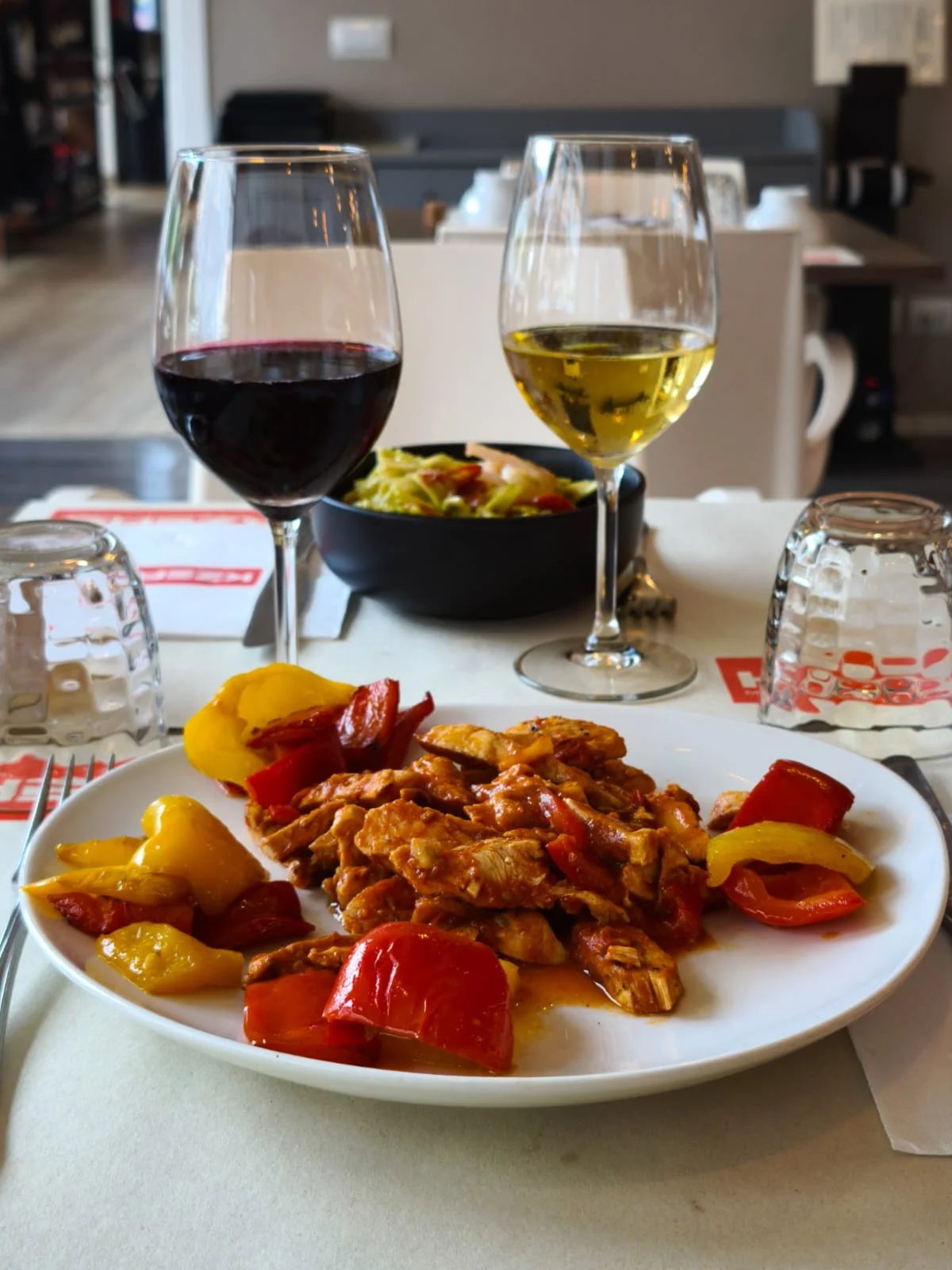Un secondo piatto con verdure e calici di vino al tavolo